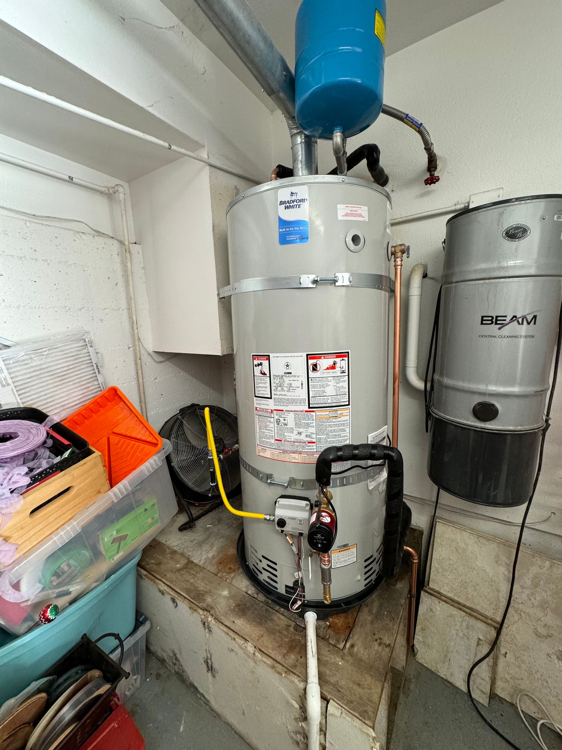 A water heater is sitting in a room next to a vacuum cleaner.