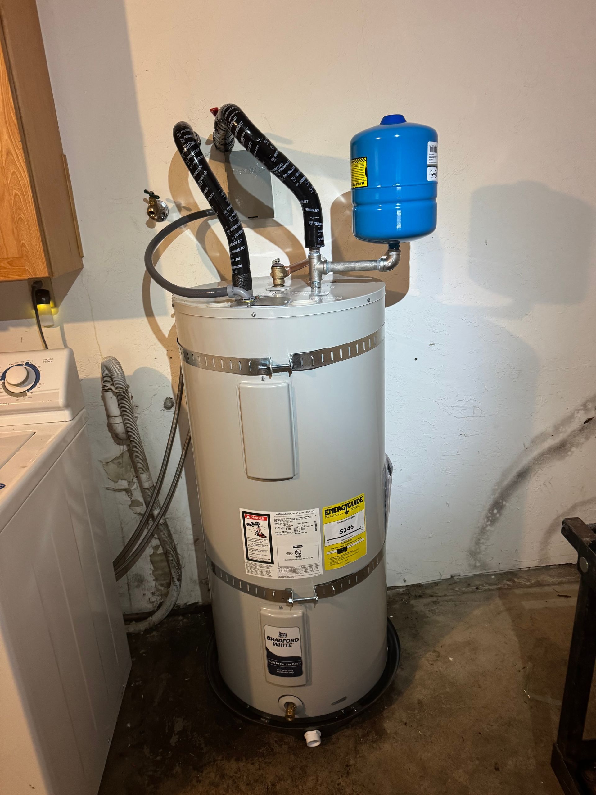 A water heater is sitting in a laundry room next to a washer and dryer.