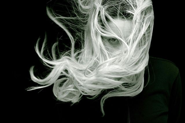A woman with long white hair covering her face in a black and white photo