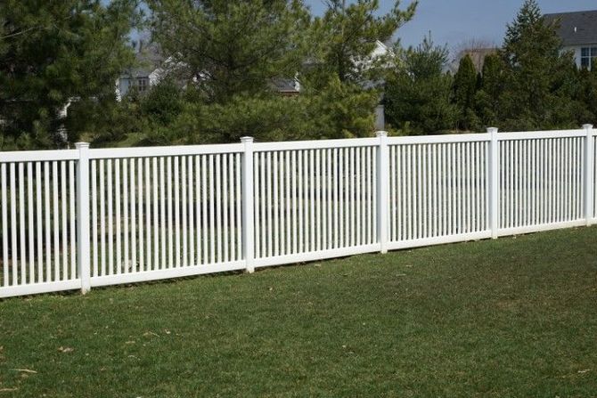 White picket fence along a grassy yard with trees in the background