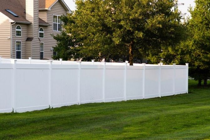 White vinyl fence along a green lawn beside suburban houses and trees