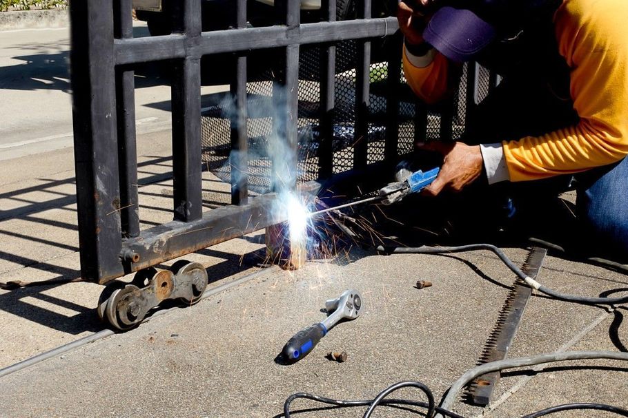 Person welding a metal gate outdoors, with bright sparks and smoke rising.