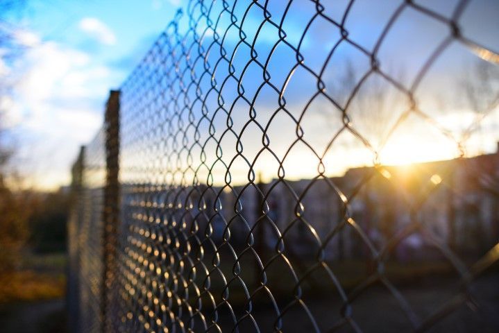 Chain-link fence at sunset with blurred buildings and blue sky in the background