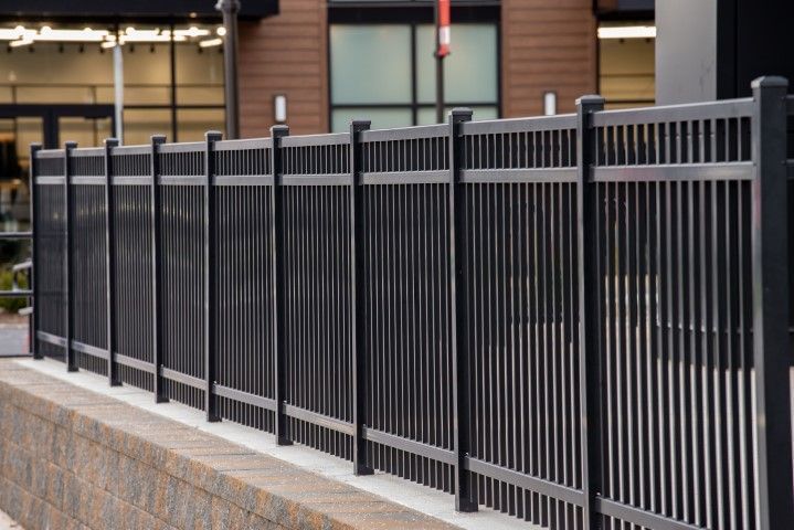 Black metal fence with vertical bars along a stone wall in an outdoor urban setting