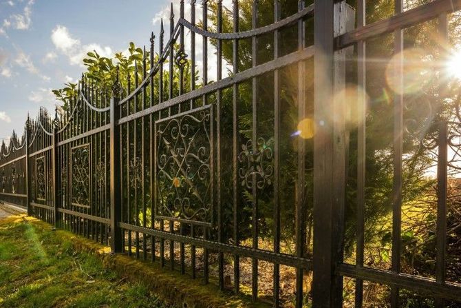Wrought-iron fence along a sunlit grassy path with trees and warm evening light