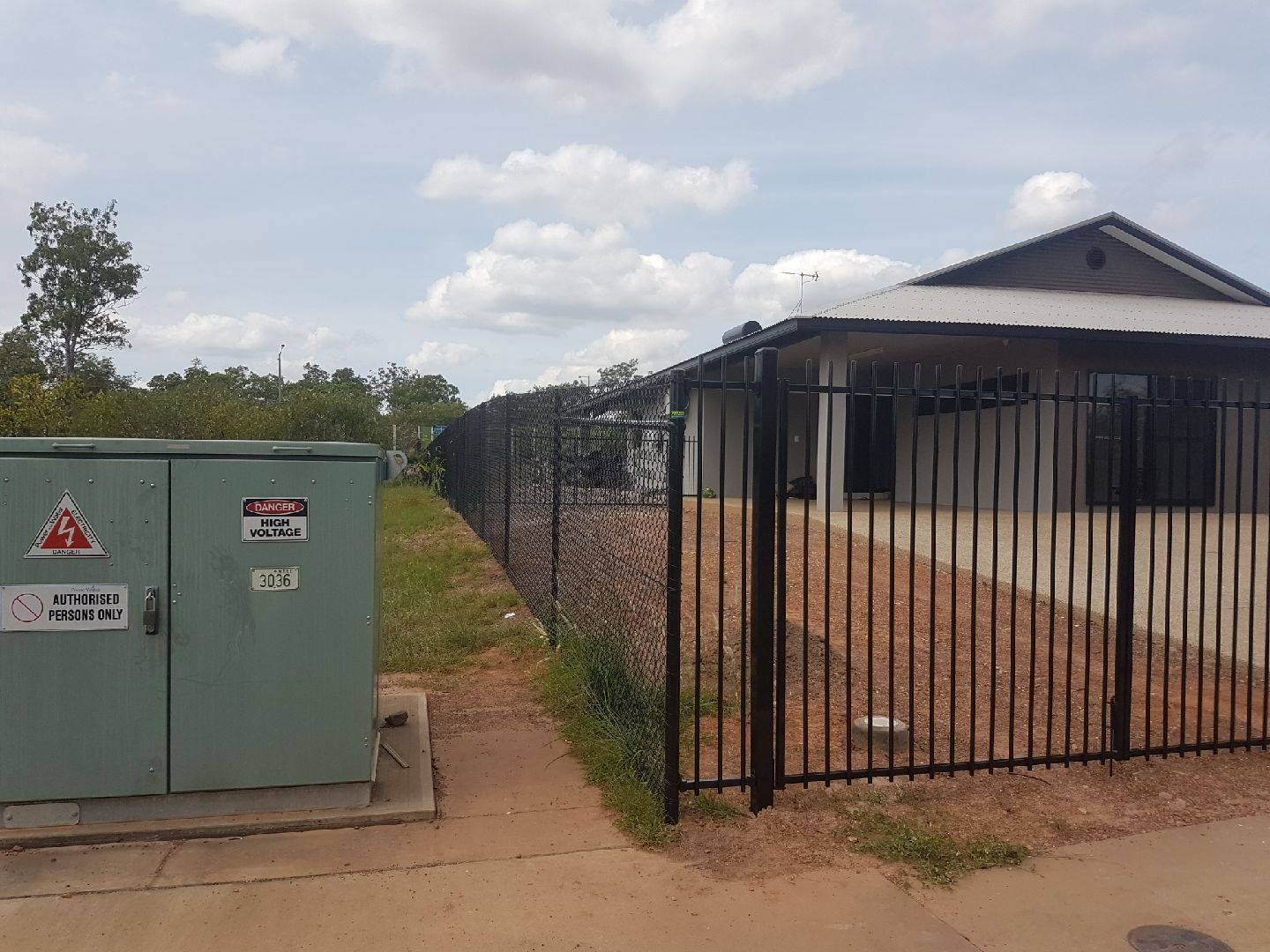 Metal fence bordering a house and utility box, with gravel path, overcast sky. — Fence Factory in Berrimah, NT