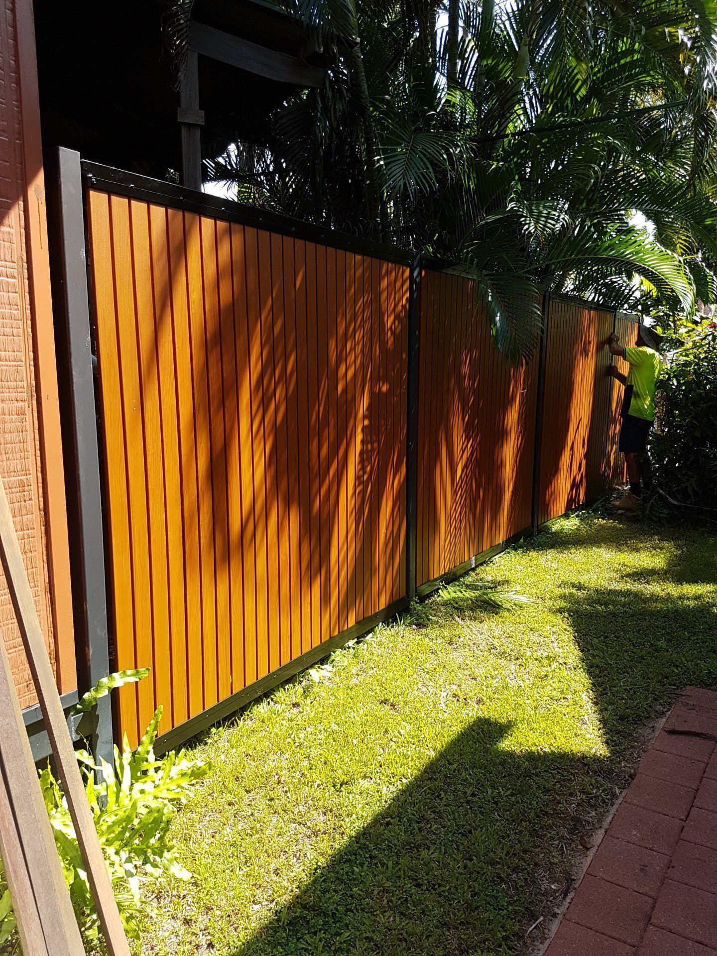 A Brick Wall with A Metal Fence Surrounded by Green Bushes — Fence Factory In Berrimah, NT