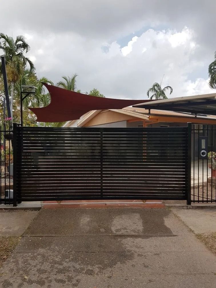 A Black Fence With a Red Sail in Front of a House — Fence Factory In Berrimah, NT
