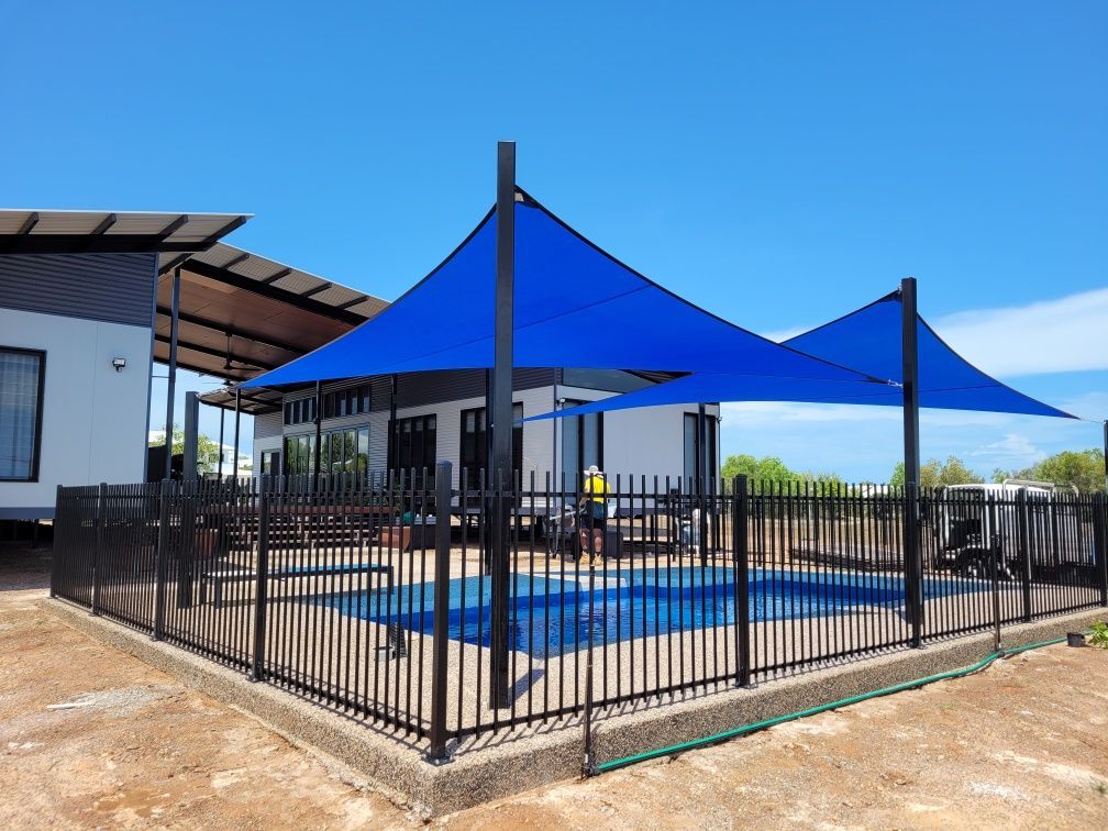 A View of A Swimming Pool with blue shade sails and a black metal fence — Fence Factory In Katherine, NT
