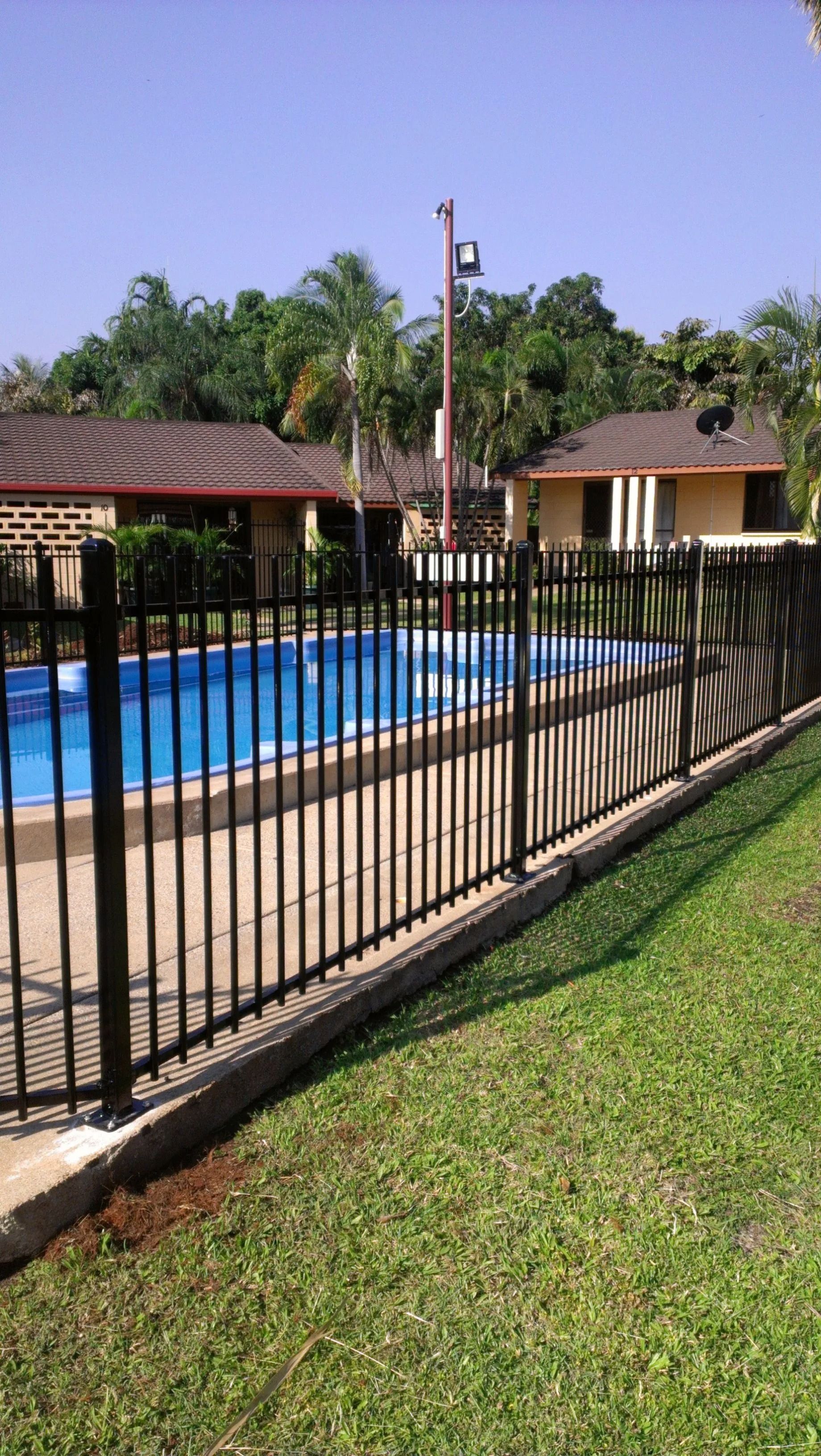 A Fence Surrounds a Swimming Pool With a House in the Background — Fence Factory In Berrimah, NT