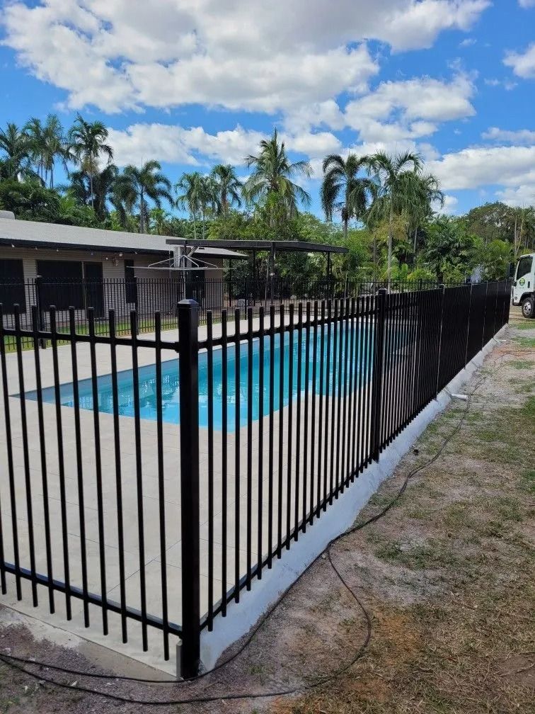 A Black Fence Surrounds a Swimming Pool in Front of a House — Fence Factory In Berrimah, NT