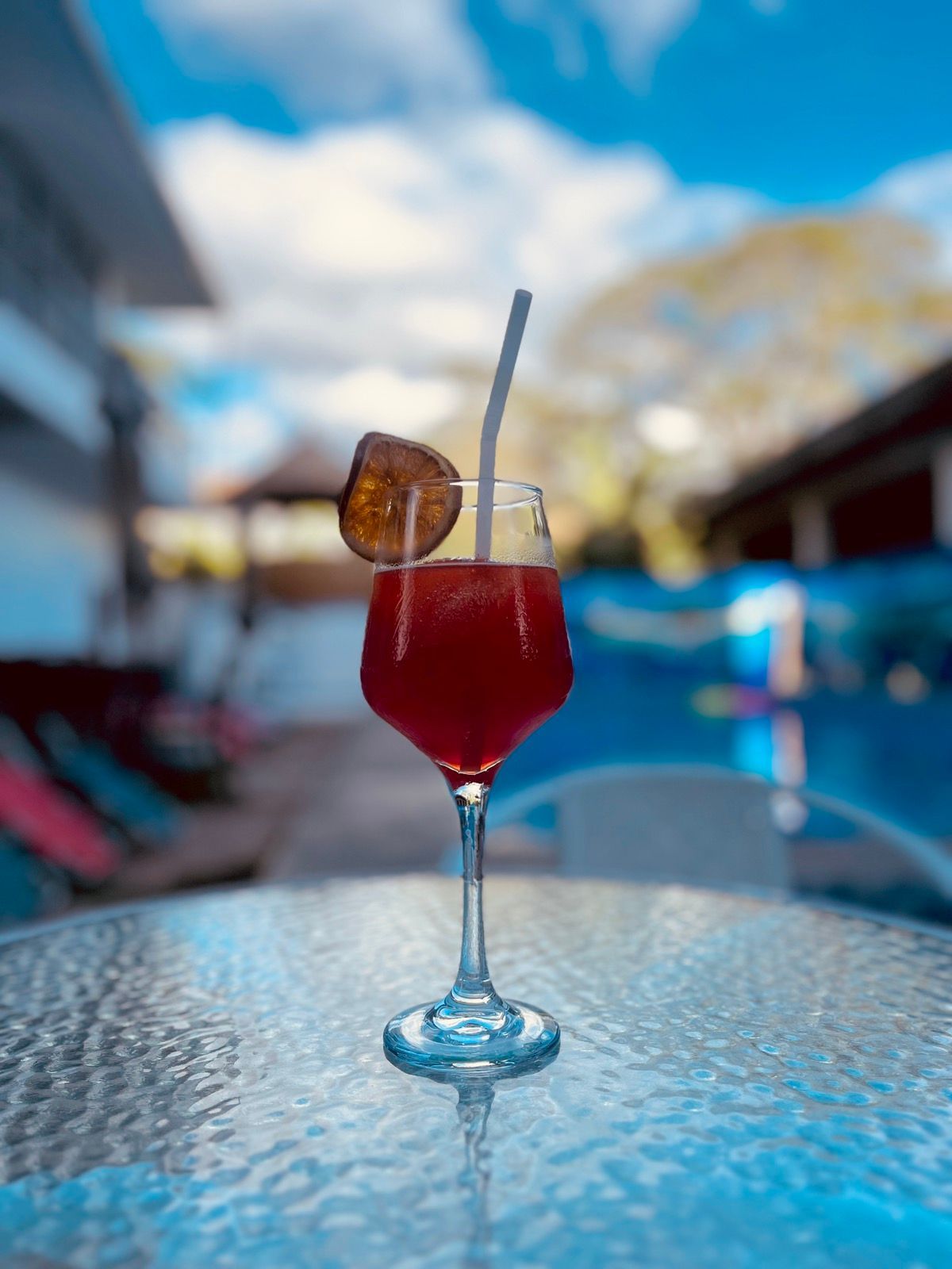 A red drink in a wine glass with a straw on a table.