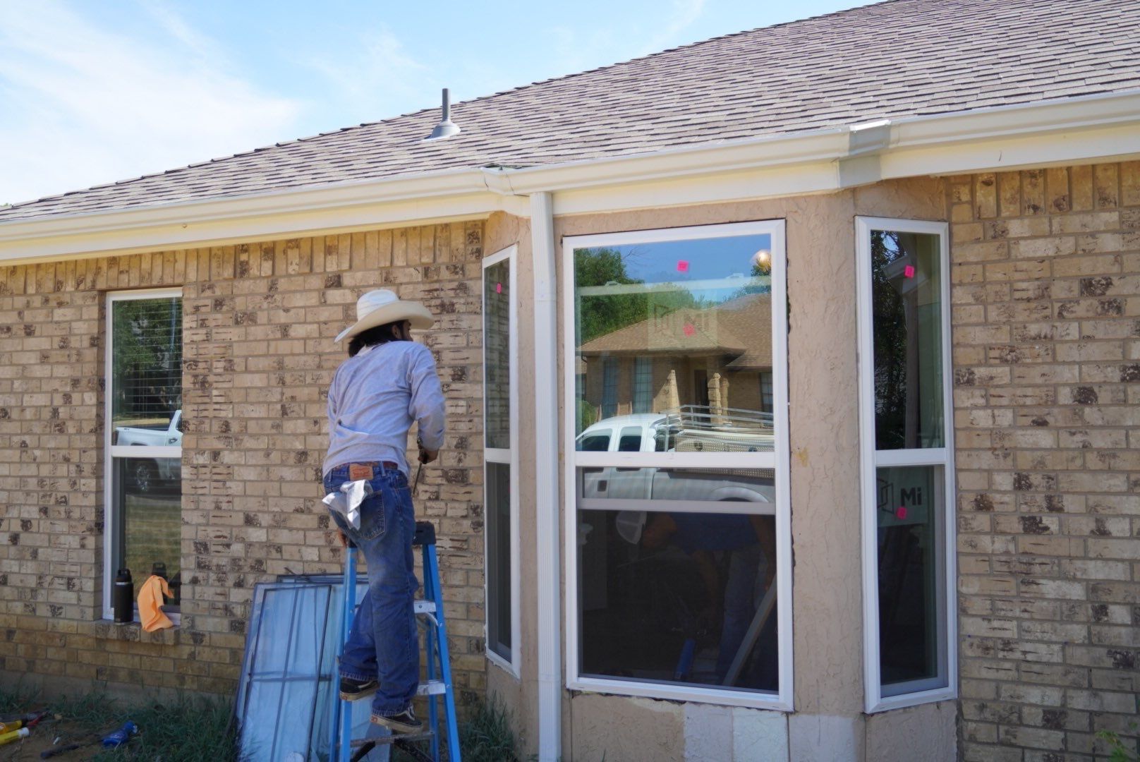Worker on a ladder painting the exterior of a brick house near a window.