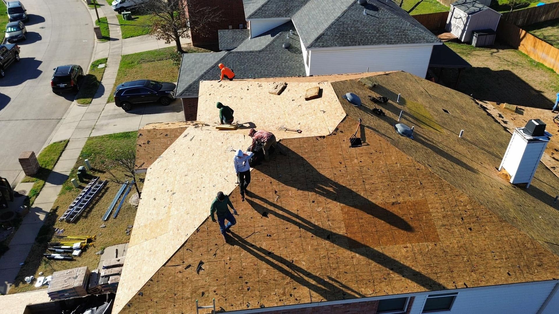 Roofers working on a shingled roof, with tools and materials, viewed from above.