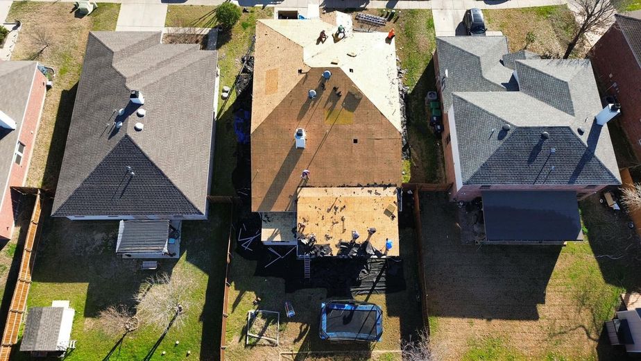 Aerial view of three suburban houses with backyards and patios in bright daylight.