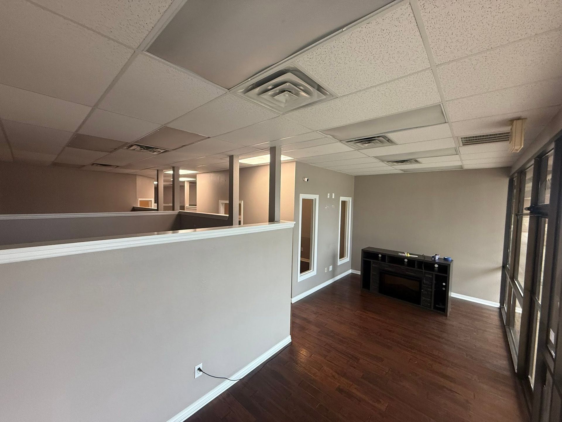 Empty office interior with white walls, wood floors, drop ceiling, and large windows.