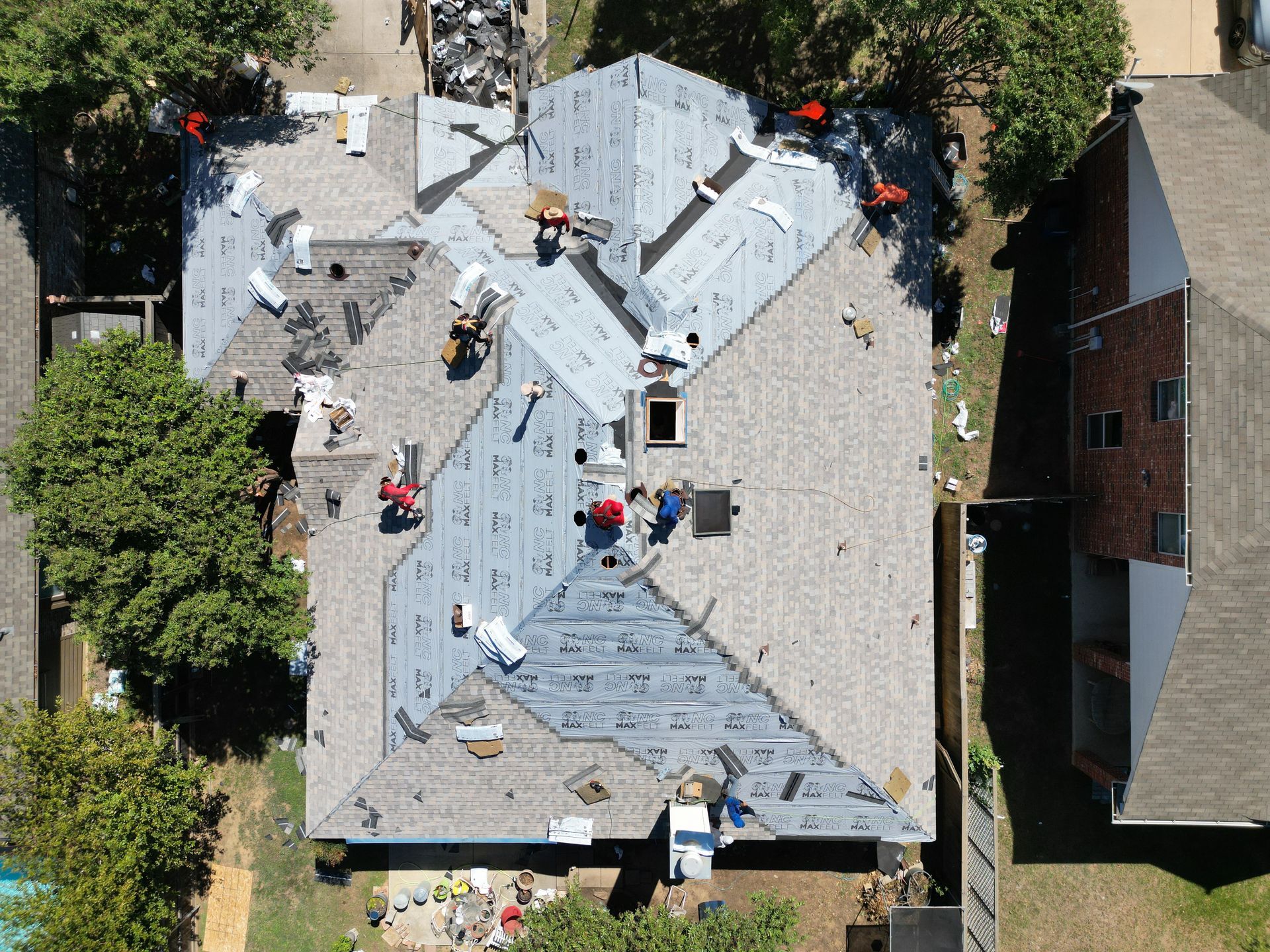 Aerial view of workers repairing a gray shingled house roof with tools and materials.