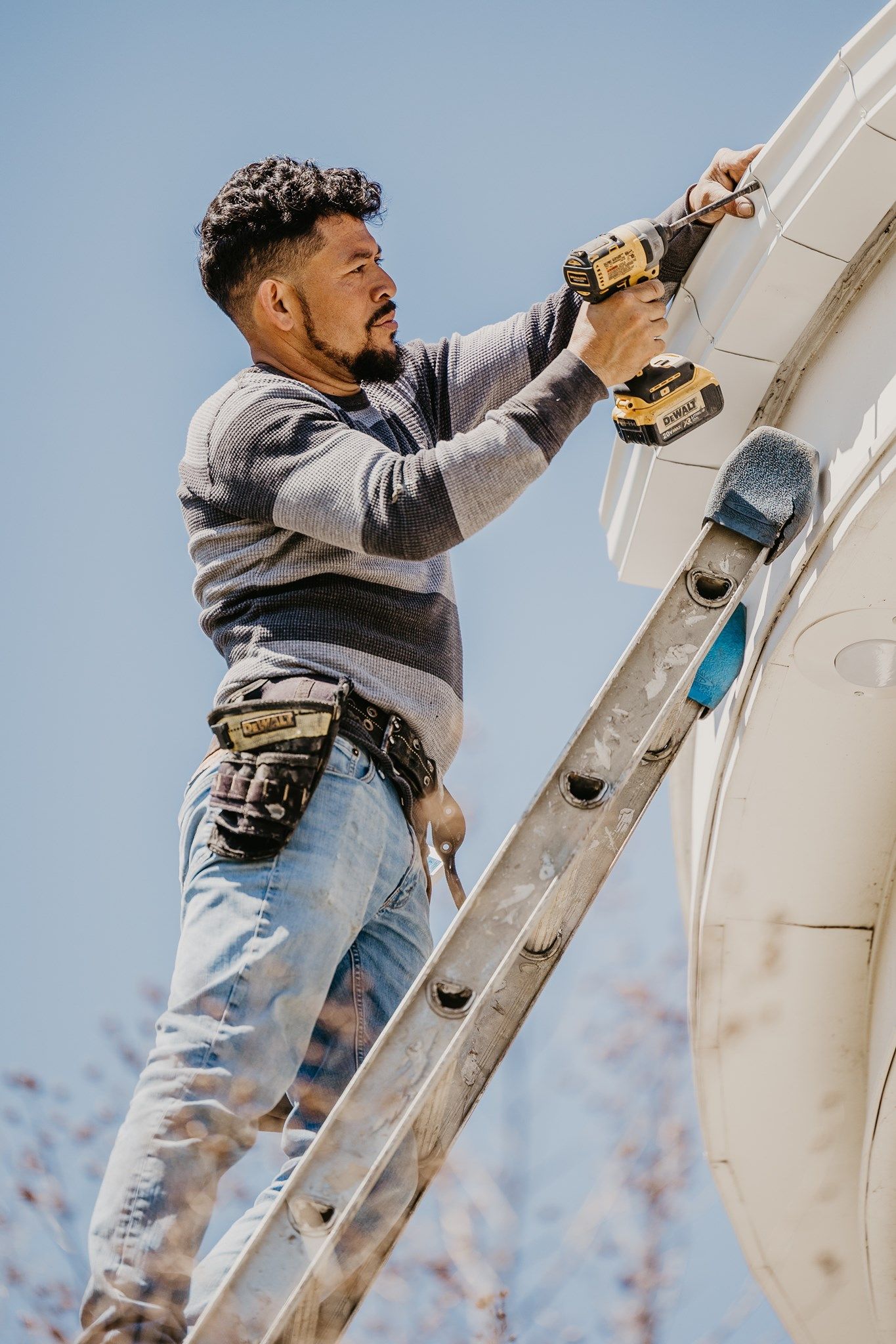 Person climbing a white extension ladder while holding tools against a pale exterior wall