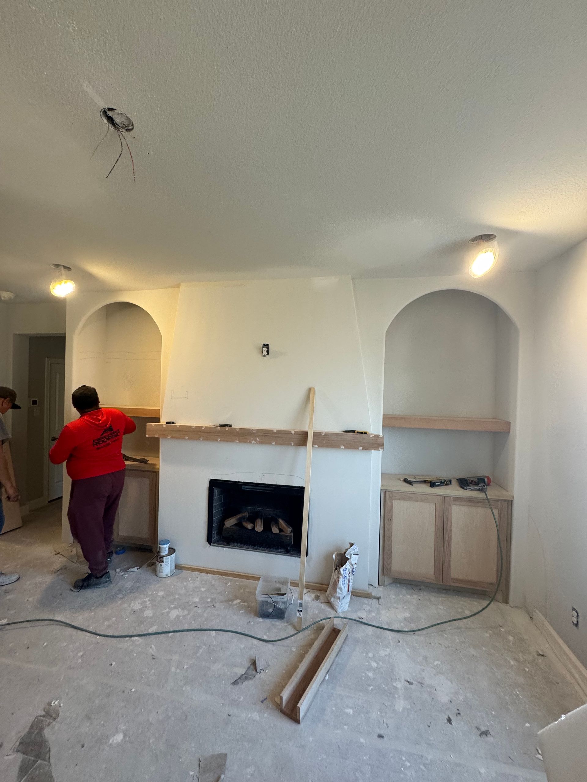 Living room under renovation with a worker in red near a fireplace and built-in alcoves