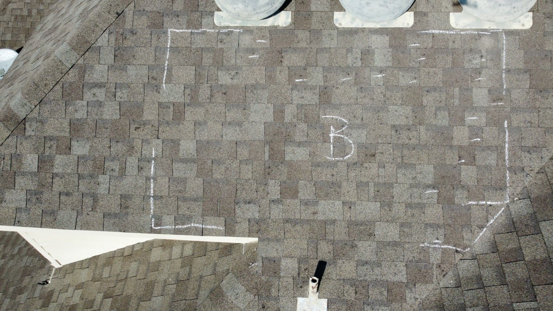 Aerial view of a gray shingled roof with skylights and a small chimney.