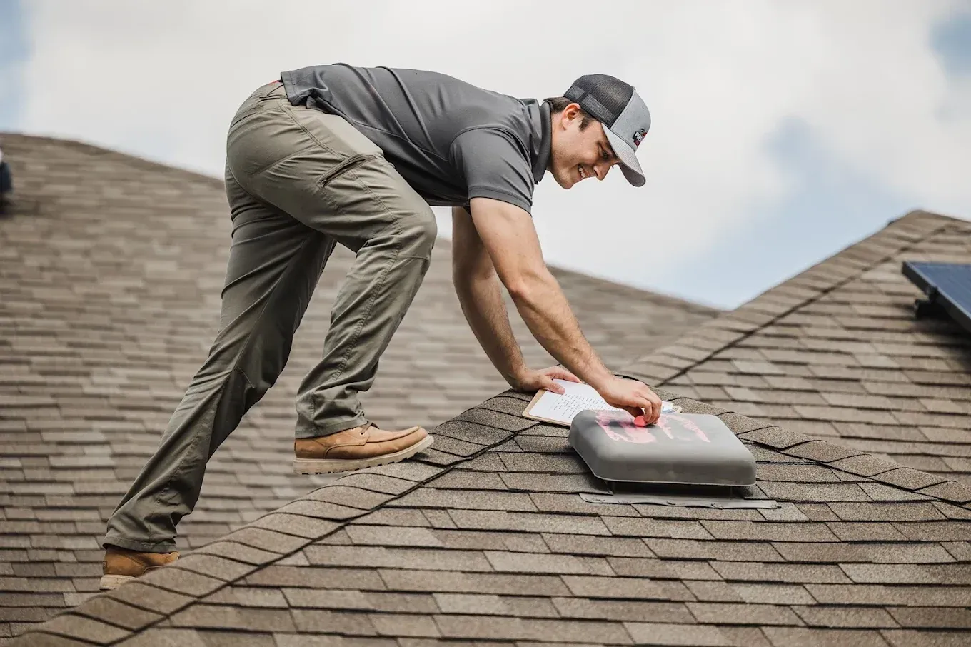 Worker cleaning roof shingles with a brush on a cloudy day