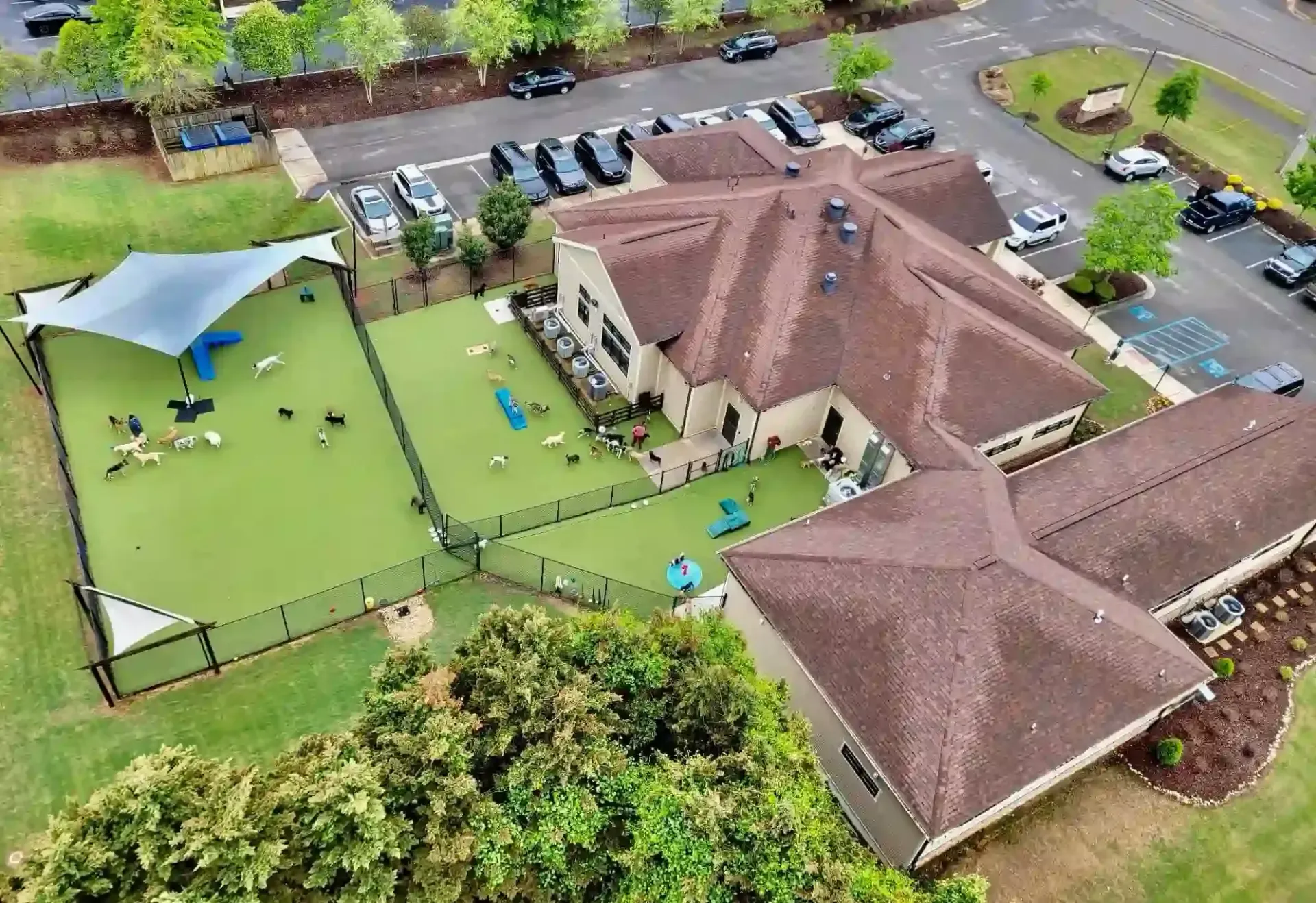Aerial view of a building with a large green play area, canopy, and parked cars nearby