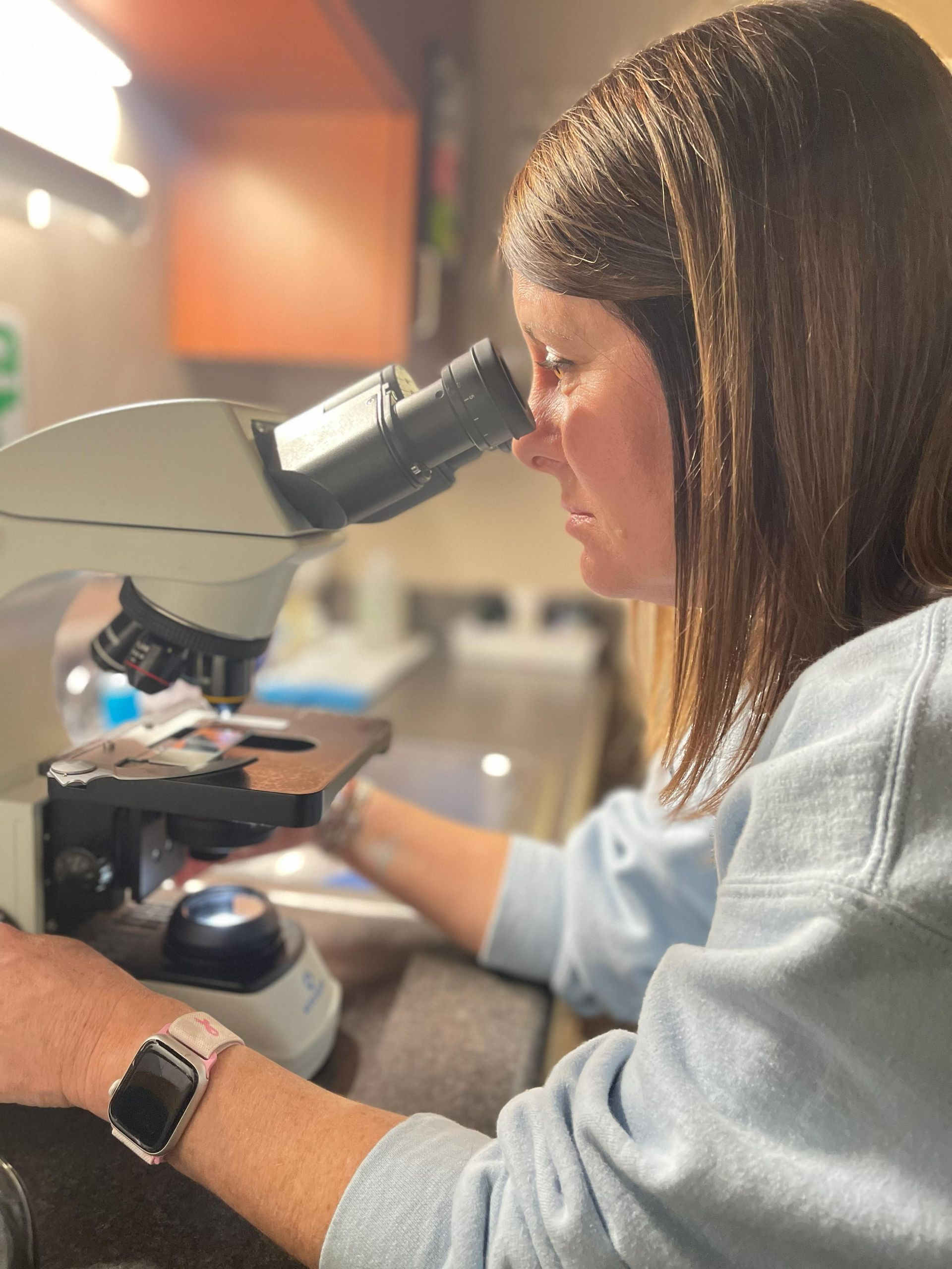 Woman using a microscope at a lab bench, examining a slide in a bright workspace