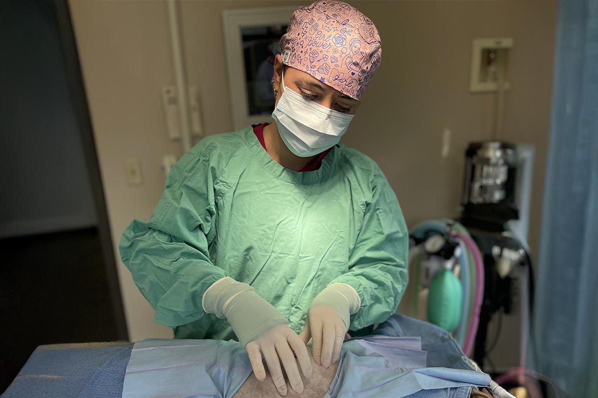 Surgical staff in green scrubs and mask prepare a patient in an operating room