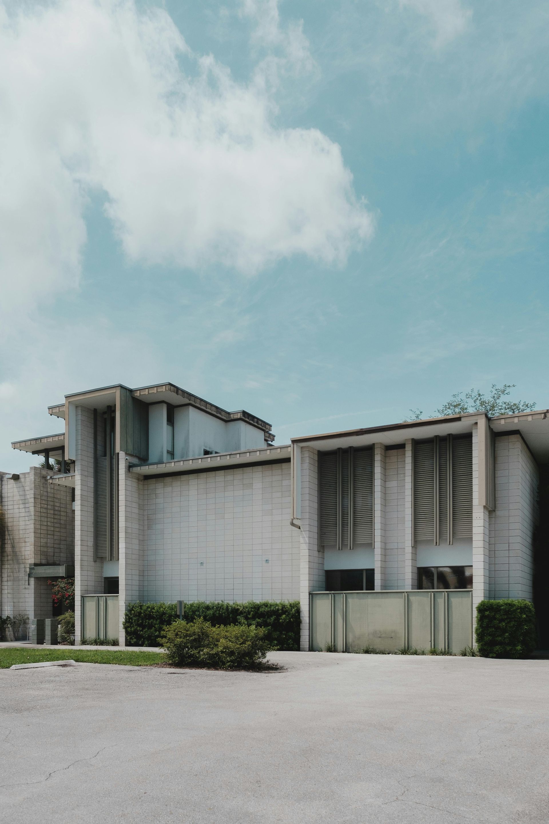 A multi-level, light-colored building with vertical slats and a flat roof under a partly cloudy sky.