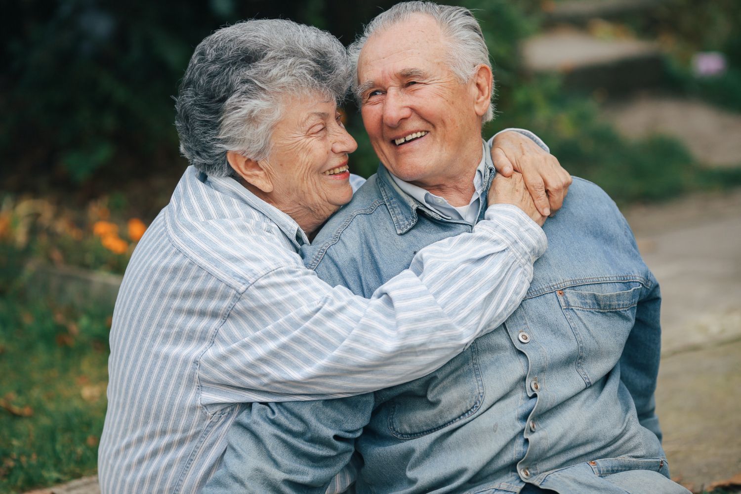 Elderly couple embracing and smiling outdoors.