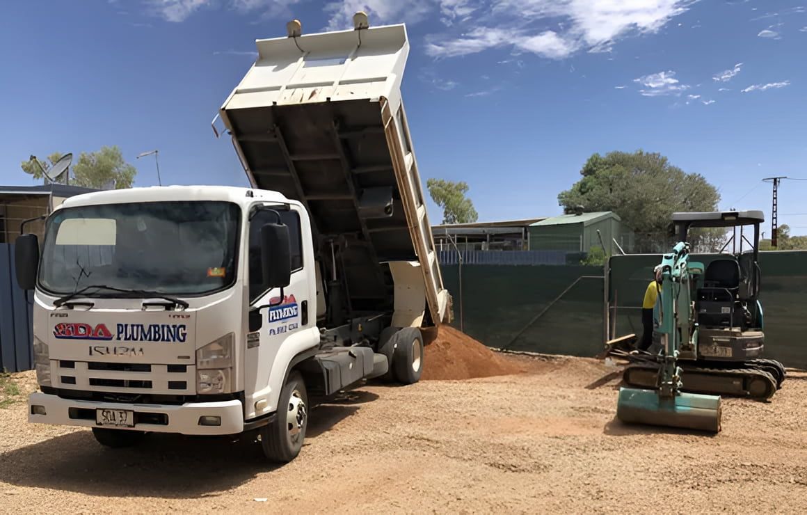 Dump Truck Unloading Dirt Near a Small Excavator on a Construction Site — SDA Plumbing in Alice Springs, NT