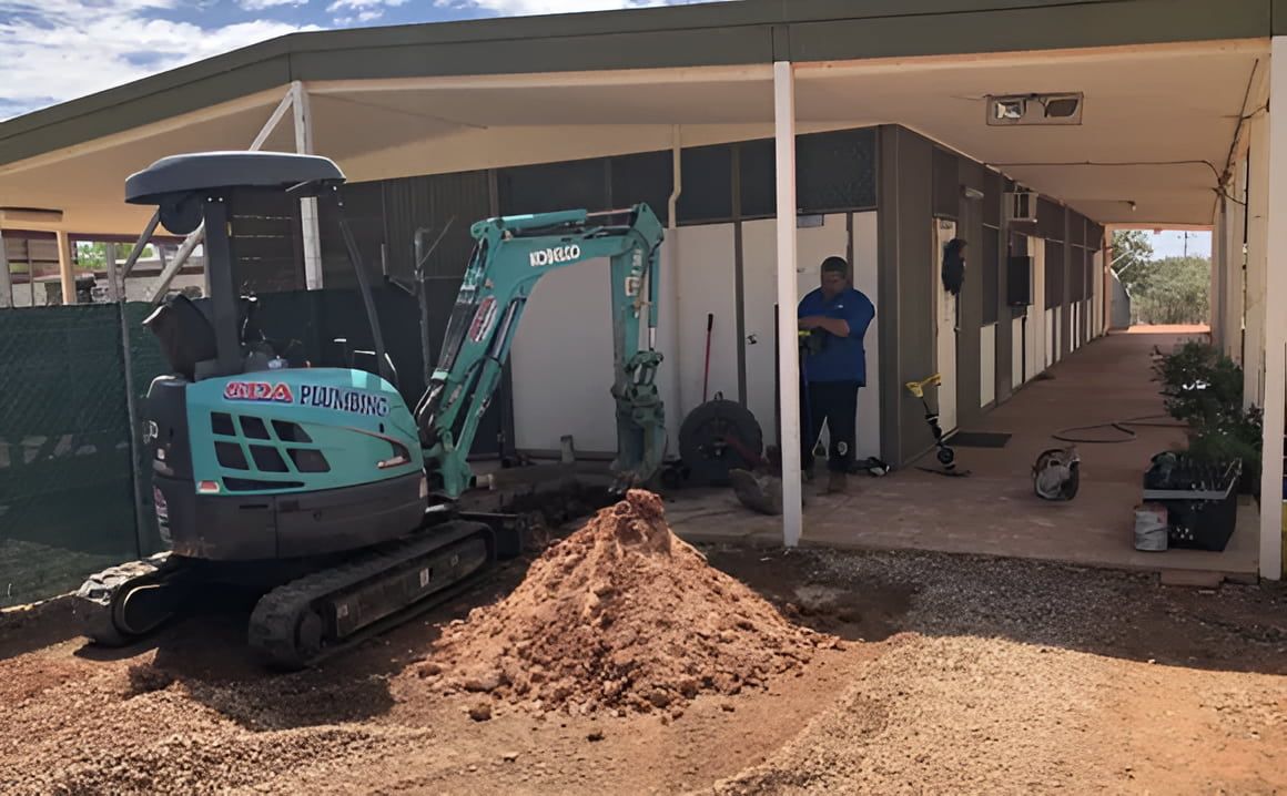 A Small Excavator Digs Near a Building — SDA Plumbing in Alice Springs, NT