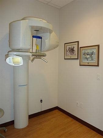 Dental X-ray machine in a small examination room with framed wall art and wood flooring