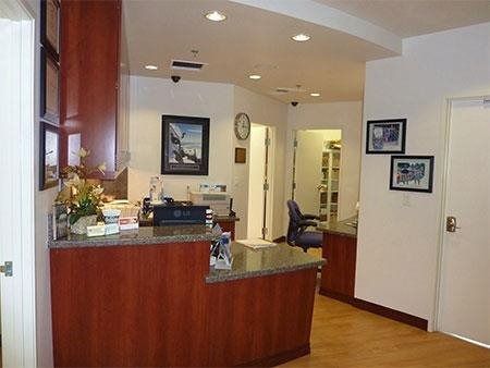 Office reception area with wood desk, hallway, framed pictures, and potted flowers