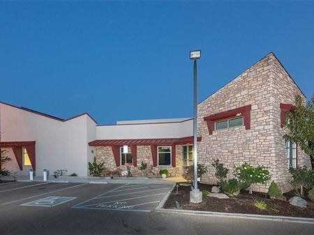 Single-story stone and stucco building at dusk with a parking lot and lamp post.