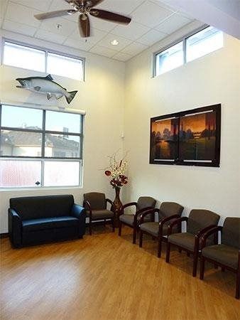 Waiting room with black couch and chairs, fish wall decor, flower arrangement, and framed sunset photo.