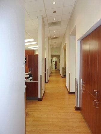 Modern office hallway with wood flooring, white walls, and glass-walled rooms.