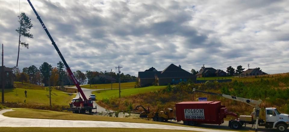 Worksite with a crane lifting a long pole beside a road under cloudy skies