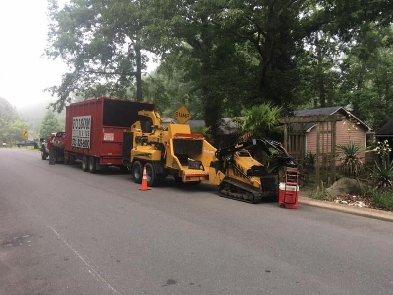 Roadside tree-trimming truck with yellow wood chipper and cones on a misty residential street