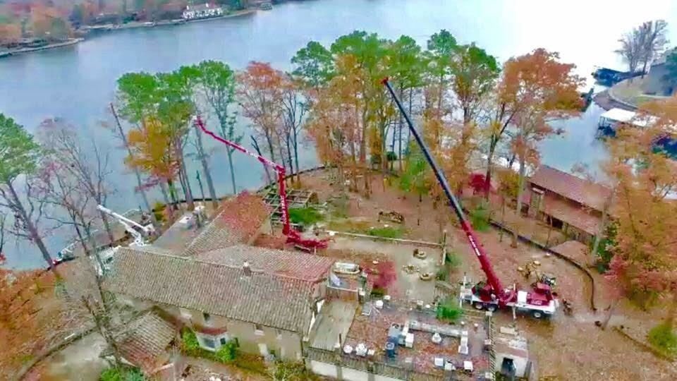 Riverfront construction site with two cranes, trees, and a building beside the water in autumn