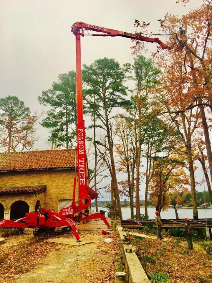 Red concrete pump truck extending boom beside a brick building in a wooded area