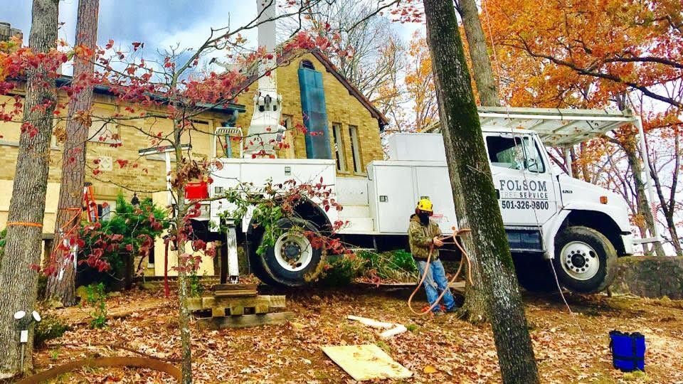 White utility truck and worker with blue bucket beside a yellow house in a leafy yard