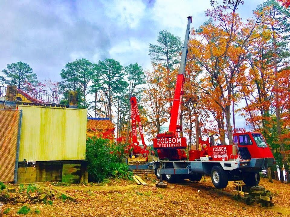 Red crane truck beside a yellow container in a wooded autumn lot