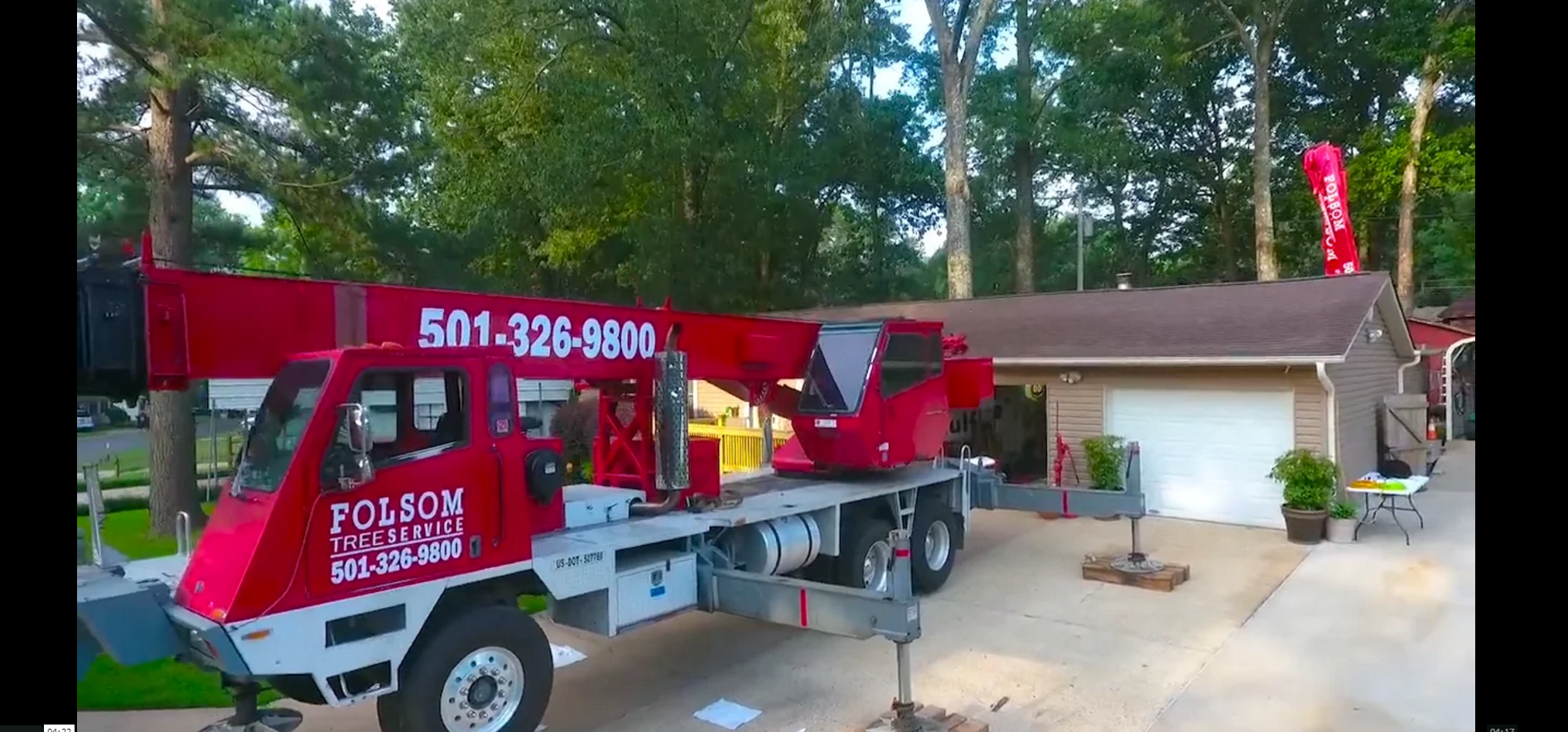 Red tow truck with crane parked in a driveway beside a house and garage