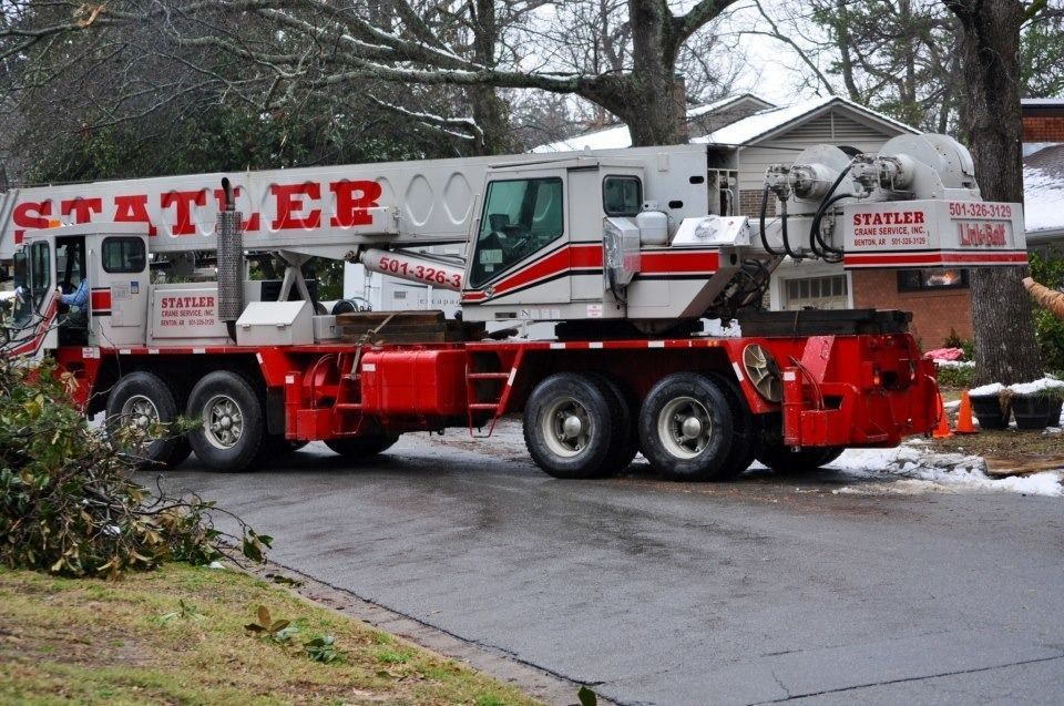 Red and white mobile crane truck on a wet road beside a building in winter.