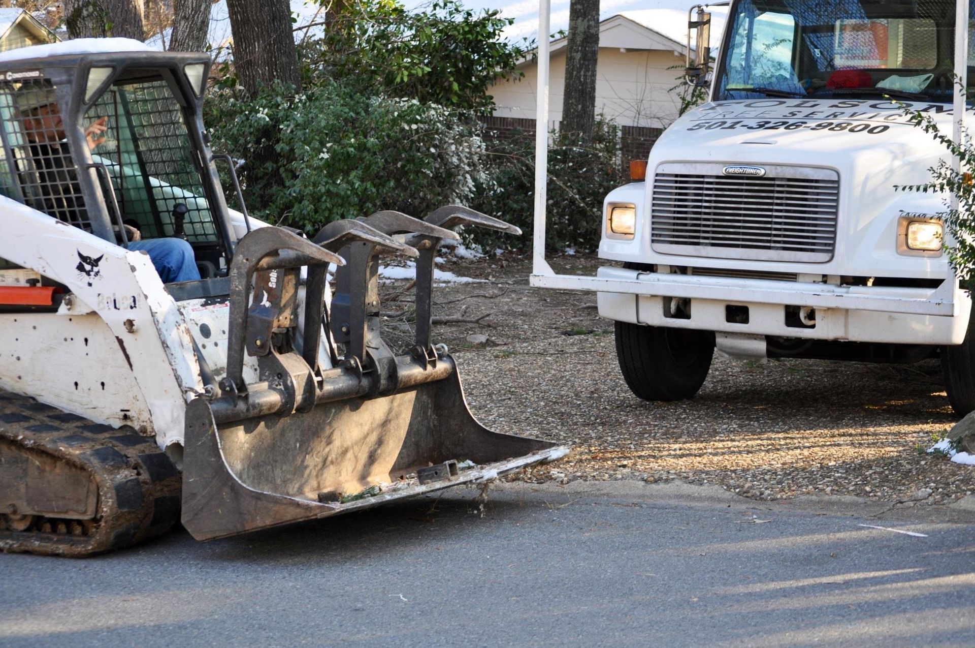 White dump truck and skid steer loader on a residential street with gravel spilled on the road