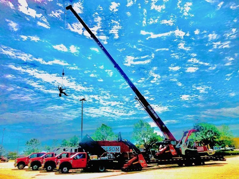 Red crane hoisting equipment beside a line of red trucks under a bright blue sky