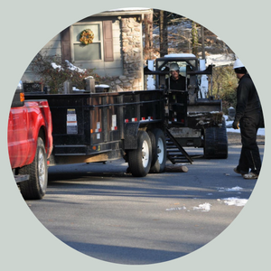 Workers moving a black trailer with a forklift beside a red pickup on a snowy street