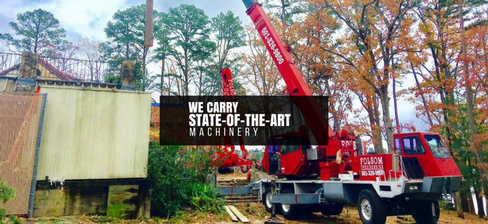 Red crane truck beside a sign reading “We carry state-of-the-art machine” in a wooded area.