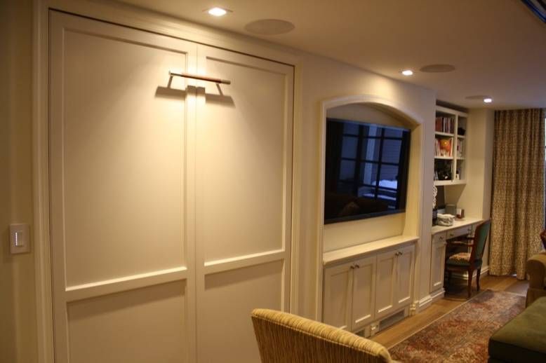 A modern living room with a fold-down wall bed, TV, and desk area with warm lighting.